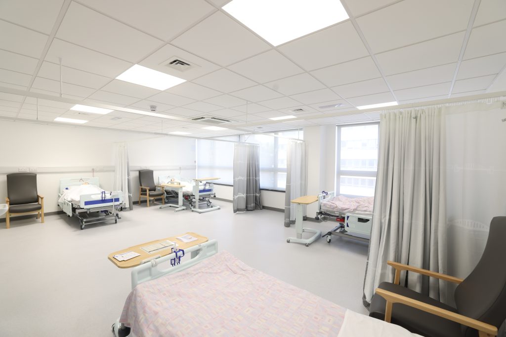 A wide angled shot of a replica hospital ward in the training centre, featuring patient beds, side tables and arm chairs.