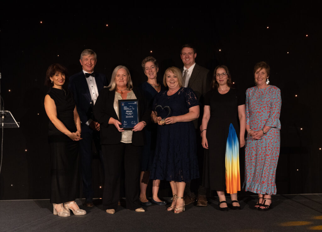 Picture of the What Matters to You Team stood on stage posing for a photo holding the award and certificate in front of star backdrop, with comedian Shaparak Khorsandi, Chairman Professor Sir John Burn and Maurya Cushlow.