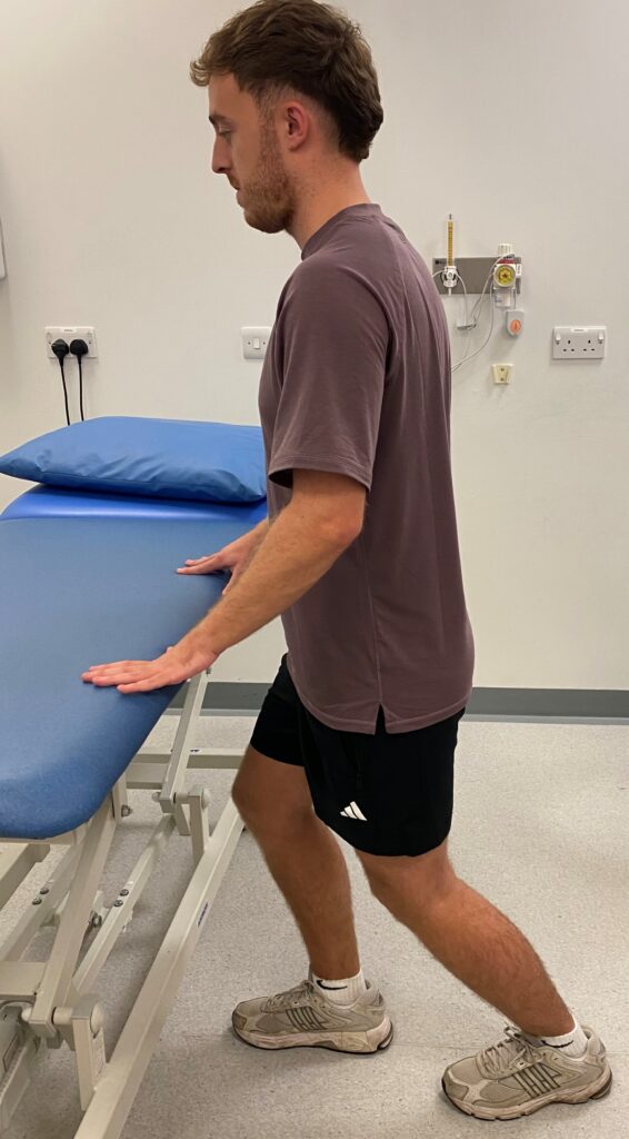 Person in walking stance facing a bed holding onto the bed,