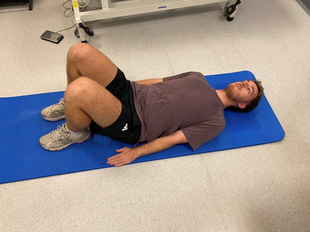 Picture of someone lying on a blue mat on their back with your knees bent and feet flat on the floor.