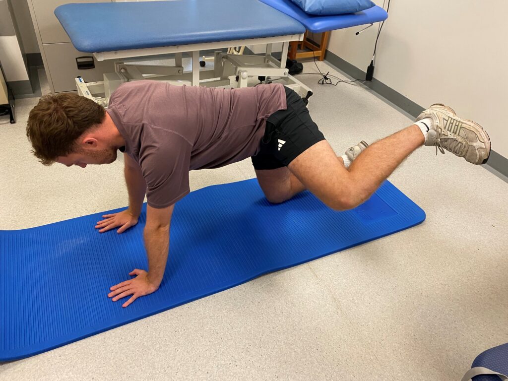 Person on all fours on a blue mat with one leg bent out and moving back towards all fours.