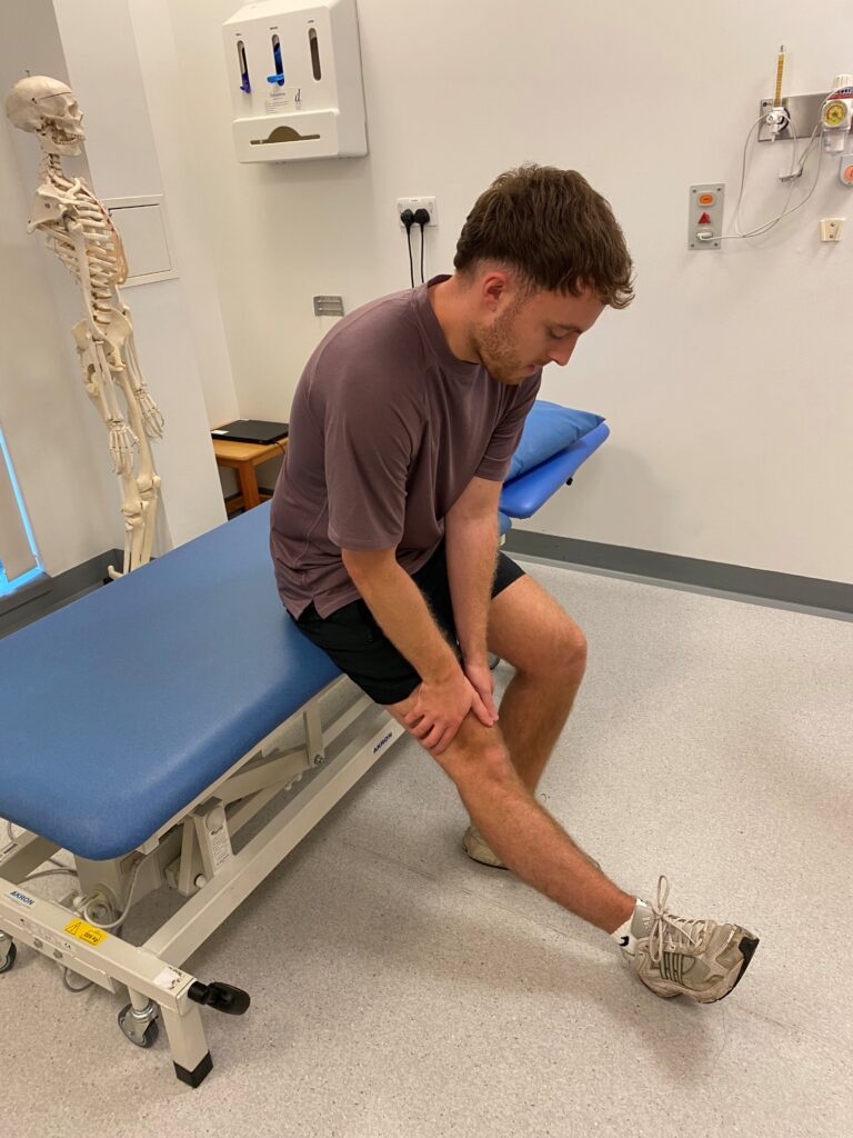 Person sat on a bed with their leg straight in front.