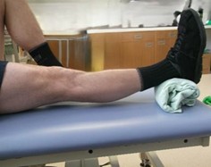 Person laid on back with one need bent and one out in front of them with a towel roll under the straight ankle.