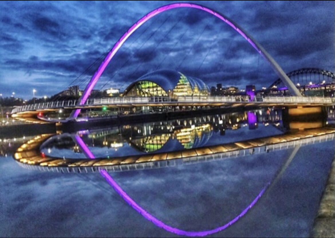 Newcastle quayside at night with the millennium bridge lit up with purple lights