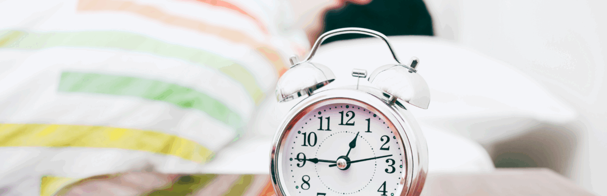 Photo of a person in bed with an alarm clock beside them