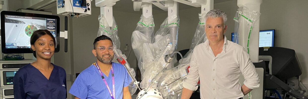 Professor Alan Horgan standing next to the robot with two surgical trainees