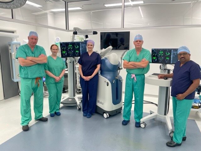 Orthopaedic surgical team, wearing scrubs and standing together in an operating theatre.