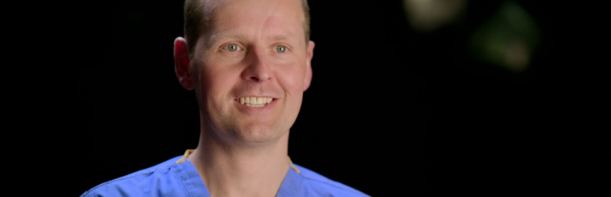 Picture of Tom Oliphant in blue scrubs smiling.
