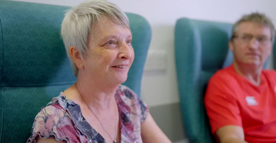 Picture of Katherine sat on turquoise chair next to Peter smiling.