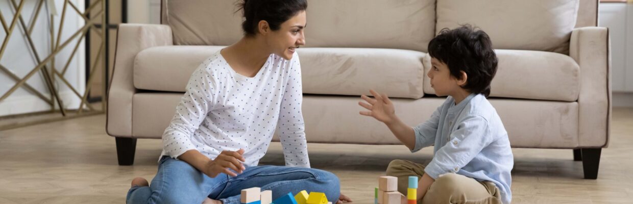 Mother and child playing together on floor, building towers from toy construction bricks, talking, enjoying leisure, playtime, creative game.