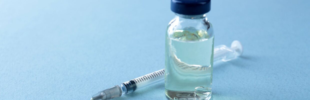 A photo of a vile of fluid with a needle placed beside it