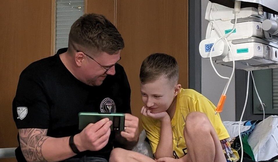 A young boy receiving treatment, his dad is showing him something on his phone