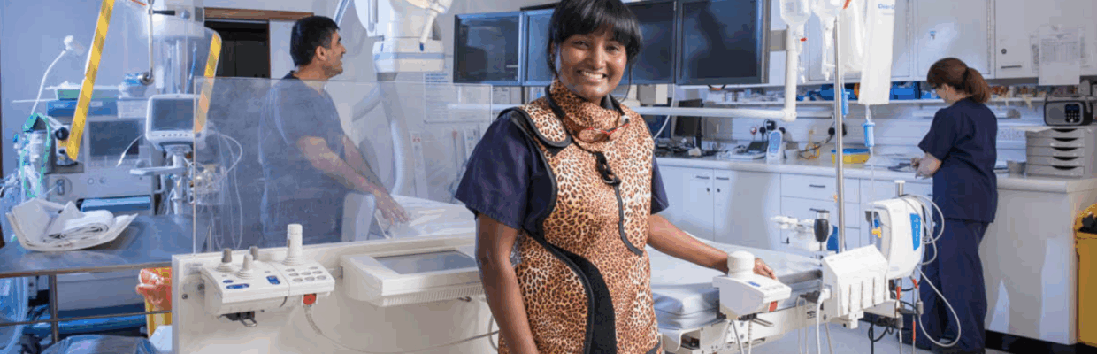 Prof Vijay Kunadian stands in a surgical theatre with two colleagues dressed in scrubs in the background.