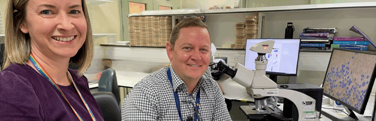 A man and a woman smiling next to a microscope with scientific image being displayed on the computer screen