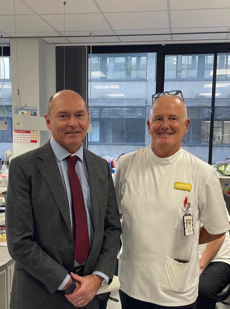 Two men in the lab, one wearing a suit and the other in lab uniform