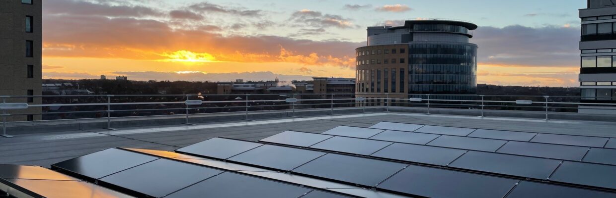 Solar panels are pictured on the roof of one of the trust's office blocks. there are 3 buildings in the background and the sun is setting