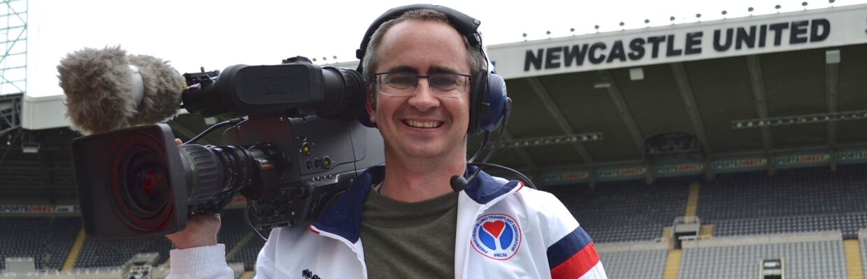 A man wearing headphones and holding a large camera in St James' Park Stadium