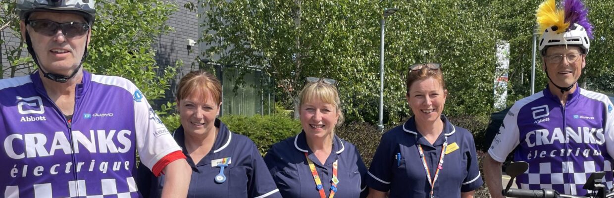 Two men sitting on bikes wearing helmets with three nurses in between them