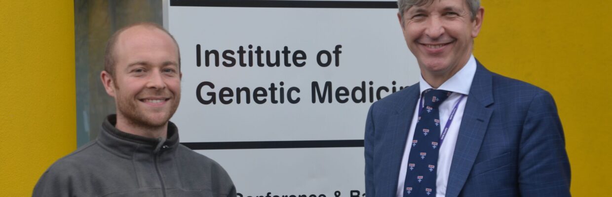 Two men standing next to Institute of Genetic Medicine sign