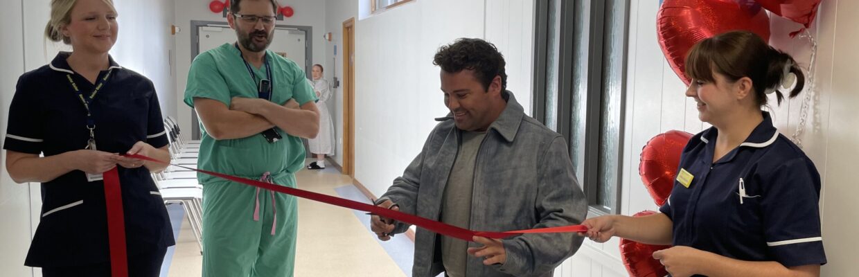 A man surrounded by hospital staff cutting a red ribbon