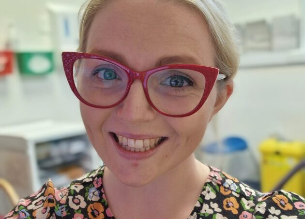 image shows a woman smiling with red glasses and a floral dress