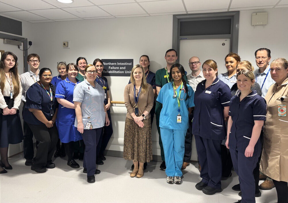 A group of clinical staff stood outside a ward with the sign for the new unit on the ward which reads "Northern intestinal failure and rehabilitation unit".