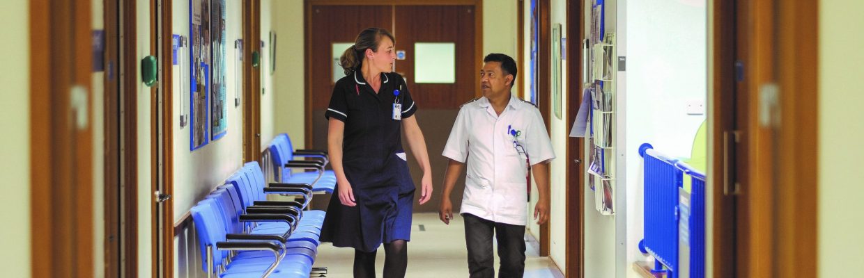 Sister and healthcare assistant walking down corridor