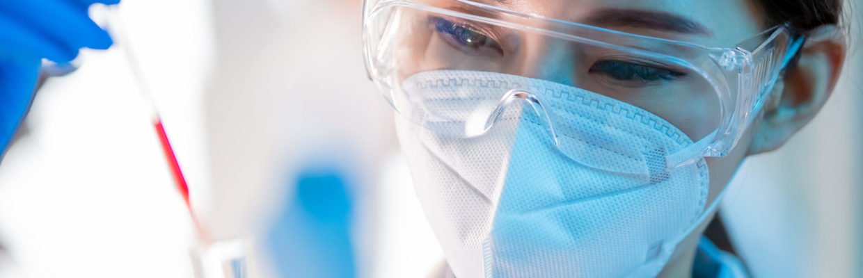 Researcher wearing PPE in a lab with a test tube.