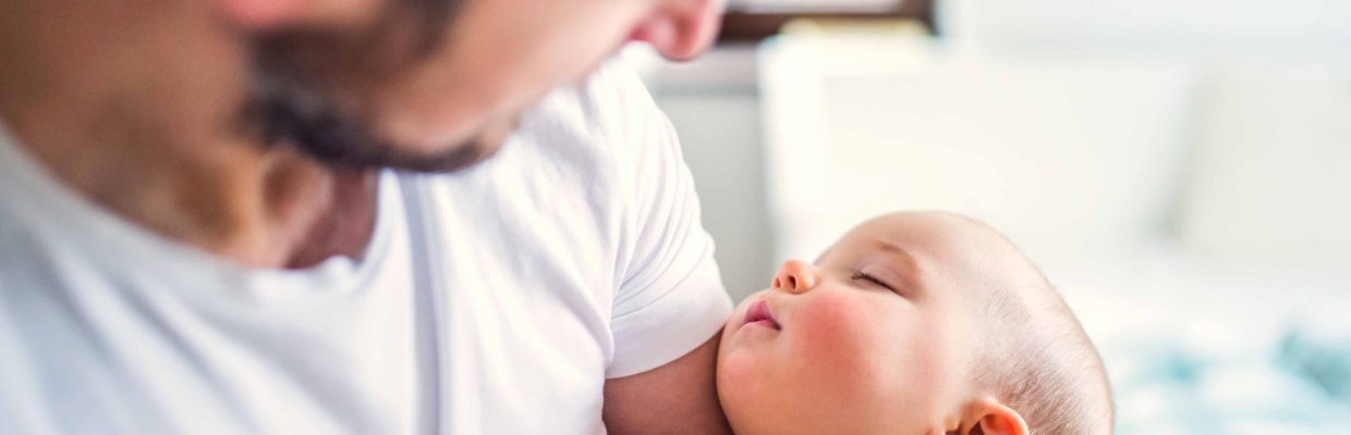 Father holding a sleeping toddler girl at home.