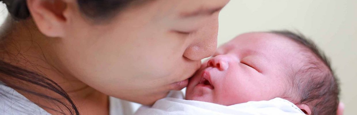 Closeup mother kissing infant baby in her arms