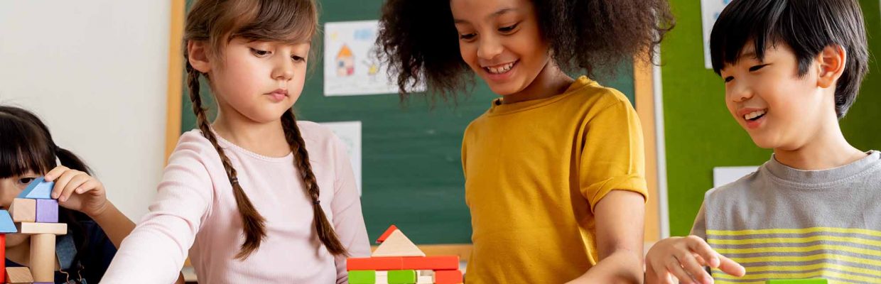 Group of multiethnic school friends using toy blocks in classroom, education, learning, teamwork. Children playing with wooden blocks in classroom