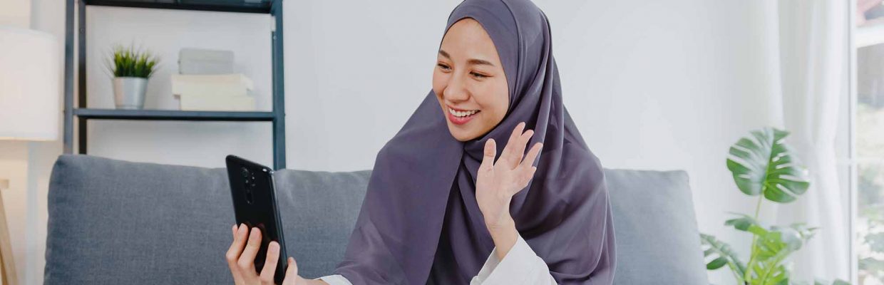 Asia muslim lady wear hijab using phone video call talking with couple at home. Young teenager making vlog video to social media on sofa in living room. Social distancing, quarantine for corona virus.