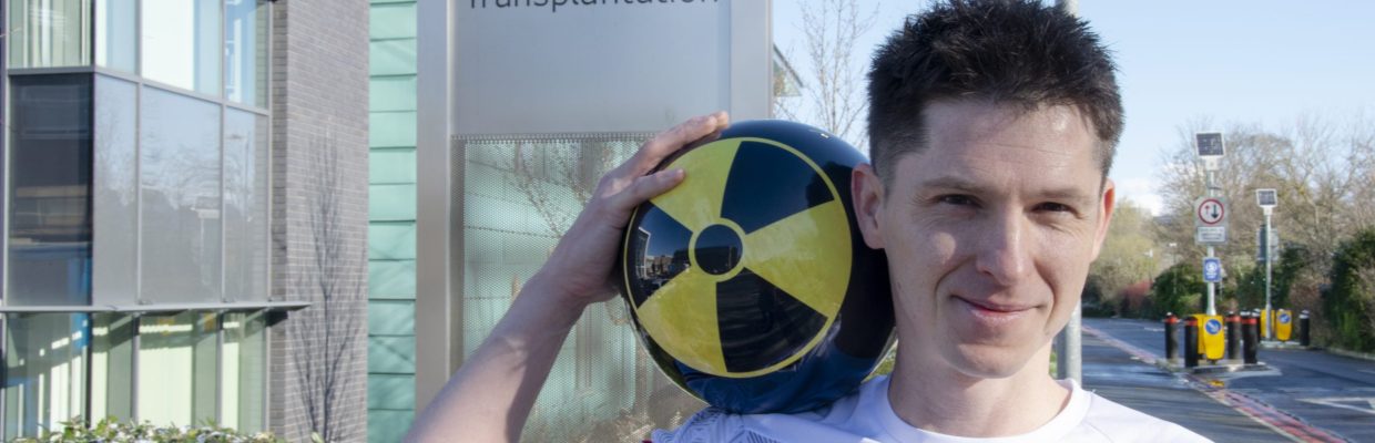 Picture of Wayne Hartley holding a black and yellow bowling ball, outside the Institute of Transplantation sign.