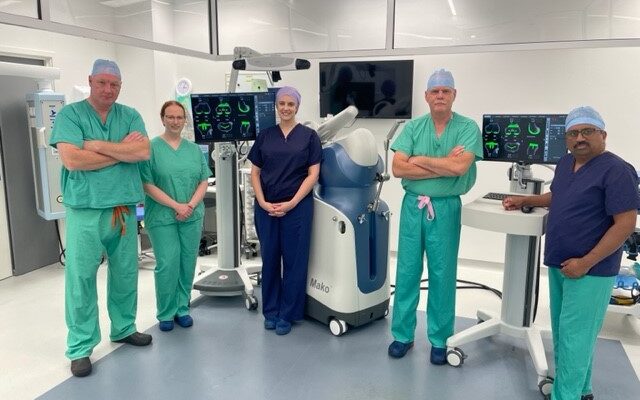 Orthopaedic surgical team, wearing scrubs and standing together in an operating theatre.
