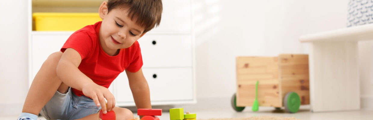 Cute little boy playing with colorful toys on floor at home.