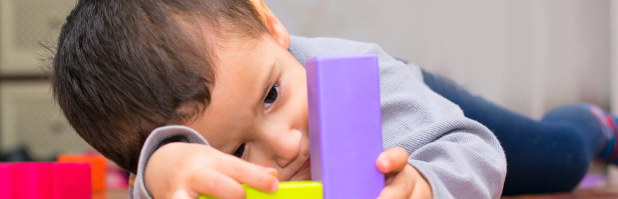 Baby lying on wooden floor playing with coloured blocks