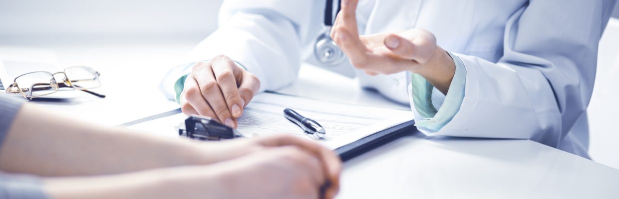 Doctor and female patient sitting at the desk and talking in clinic near window